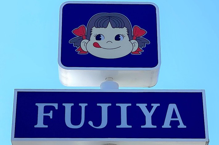A sign for Fujiya with an illustration of a girl’s face above the text “Fujiya.” The girl has a distinctive hairstyle with red ribbons