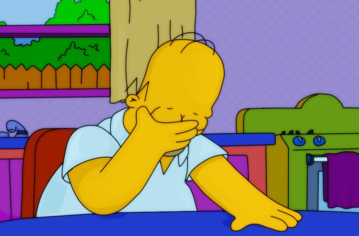 Homer Simpson facepalming at a kitchen table with a purple wall, window, and stove in the background