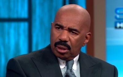 Steve Harvey wearing a suit and tie, looking puzzled during an interview