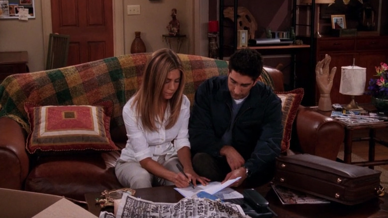Jennifer Aniston and David Schwimmer are sitting on a couch, reviewing documents together in a living room