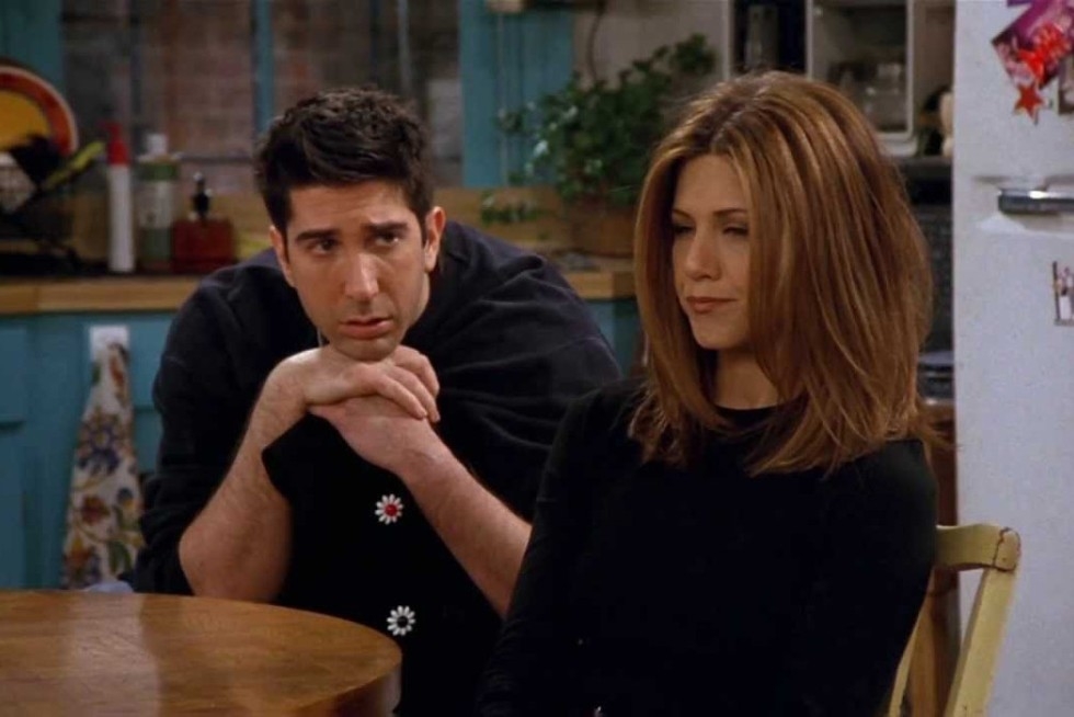 David Schwimmer and Jennifer Aniston sitting at a table, with Schwimmer looking at Aniston, from a scene in the TV show &quot;Friends.&quot;
