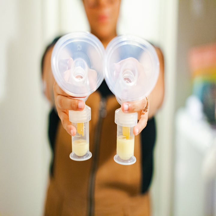 Person holding two breast pump collection containers with milk in them
