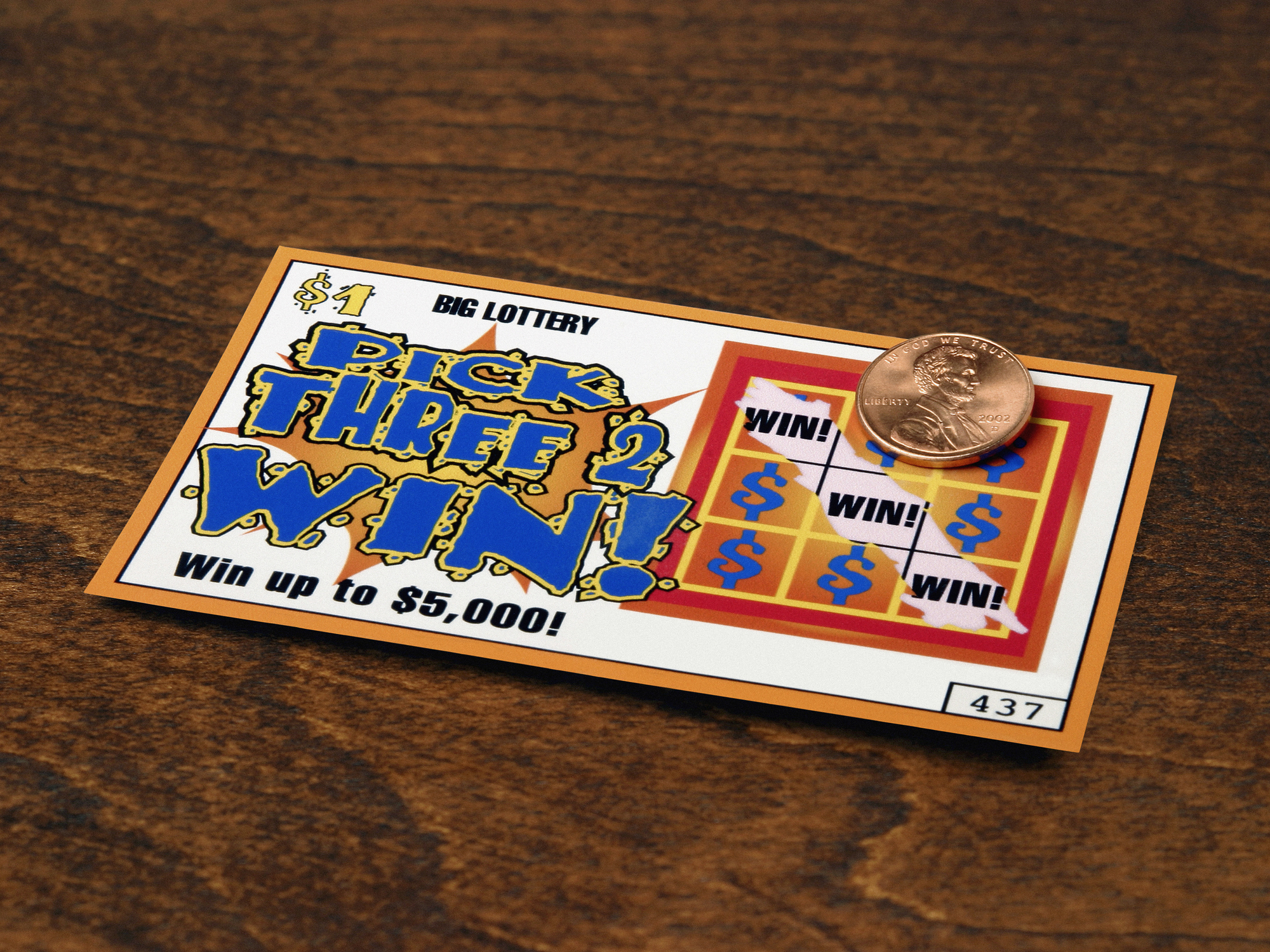 A scratched lottery ticket revealing wins, with a penny resting on it. The ticket says "Pick Three to Win! Win up to $5,000!"