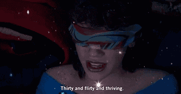 A person wearing a blindfold is seen with the text "Thirty and flirty and thriving" displayed on the screen