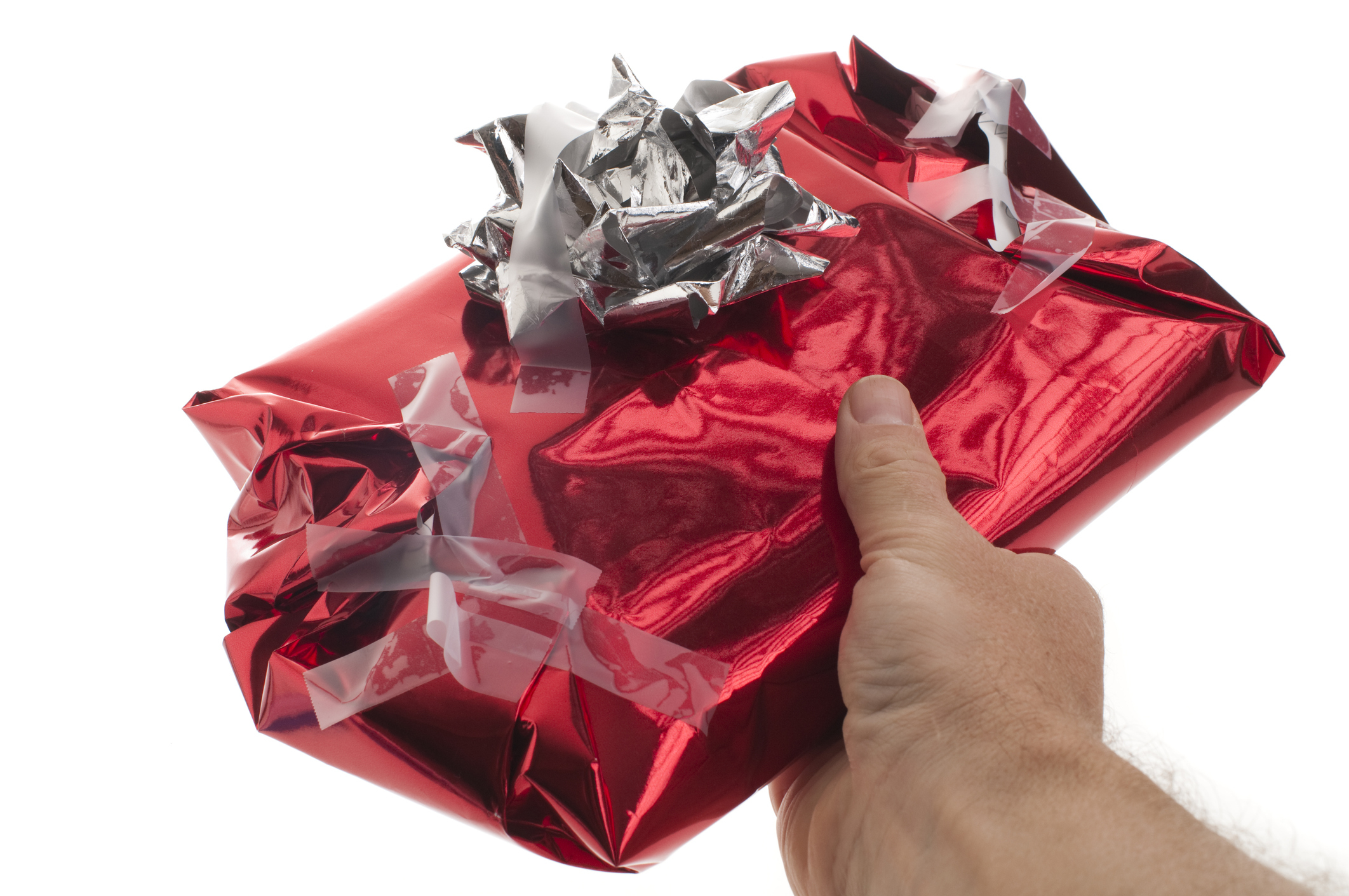 A hand holds a gift wrapped in shiny paper with a metallic bow on top