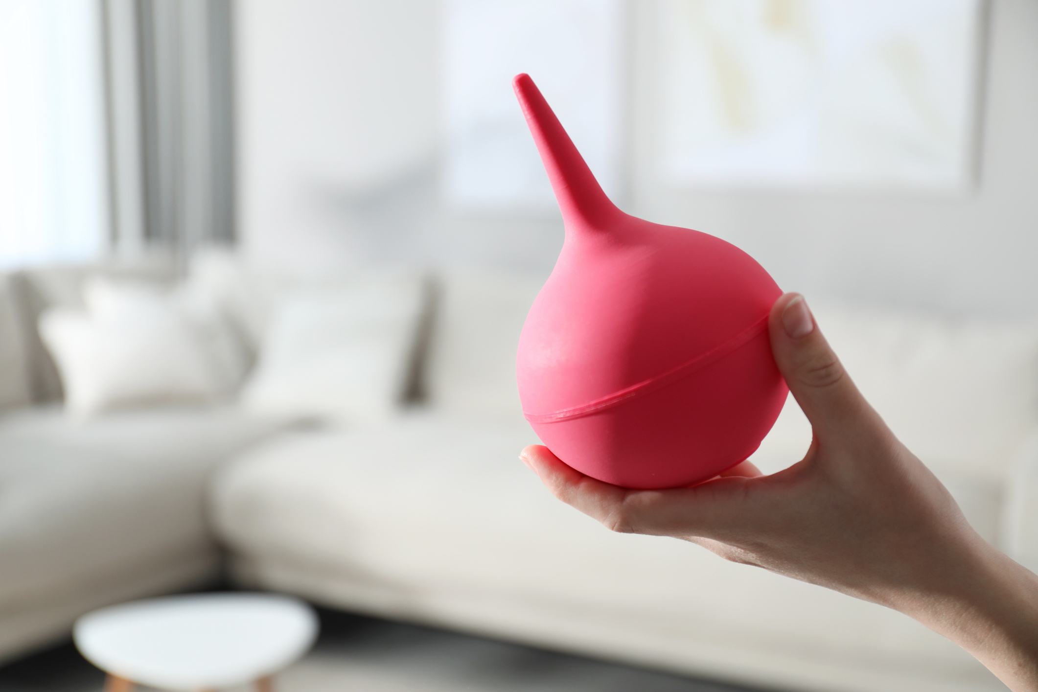 Hand holding a red enema bulb in a modern living room setting
