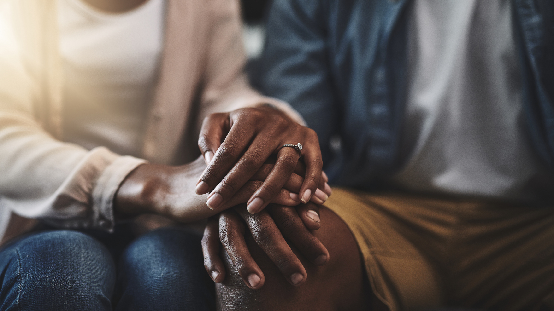 A couple holds hands closely, showing intimacy and connection. The woman wears a ring on her finger