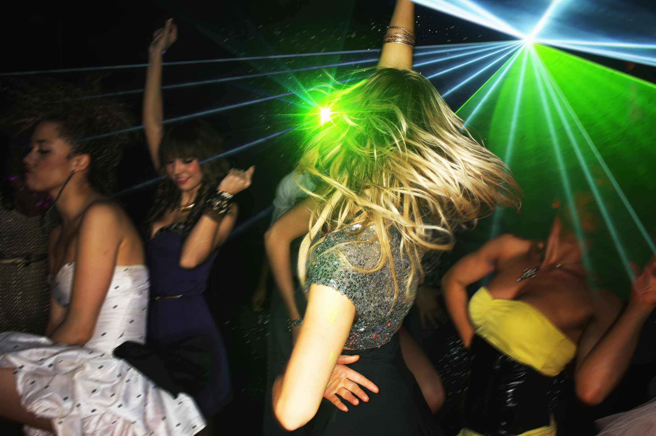 People dancing at a lively nightclub with neon lights creating a party atmosphere. The main focus is on a woman in a glittery dress spinning around with her hair flying