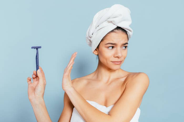 A woman with a towel wrapped around her head and body looks displeased while holding out a disposable razor