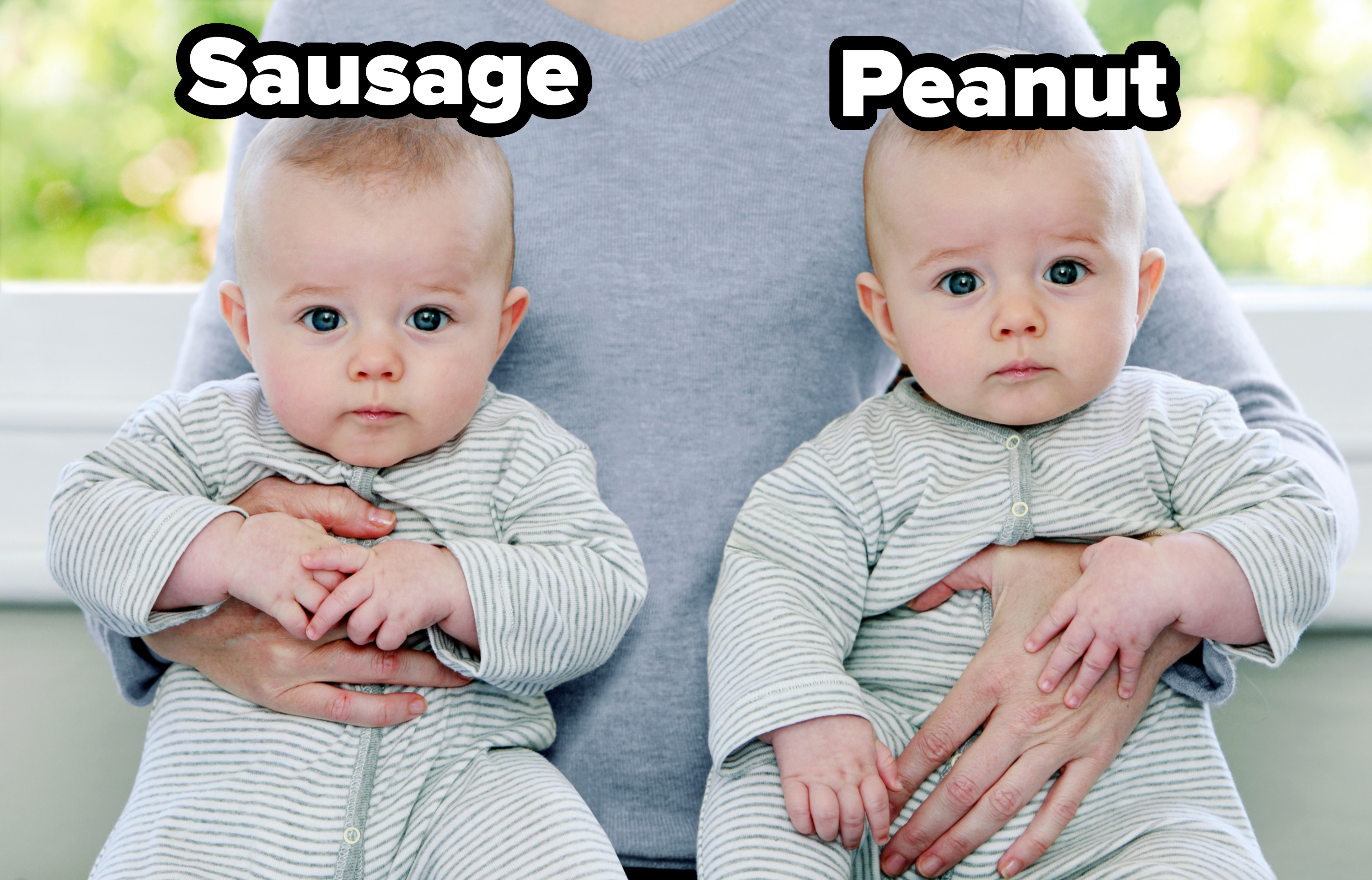 A person holds two babies dressed in identical striped outfits. The babies have serious expressions and are looking directly at the camera