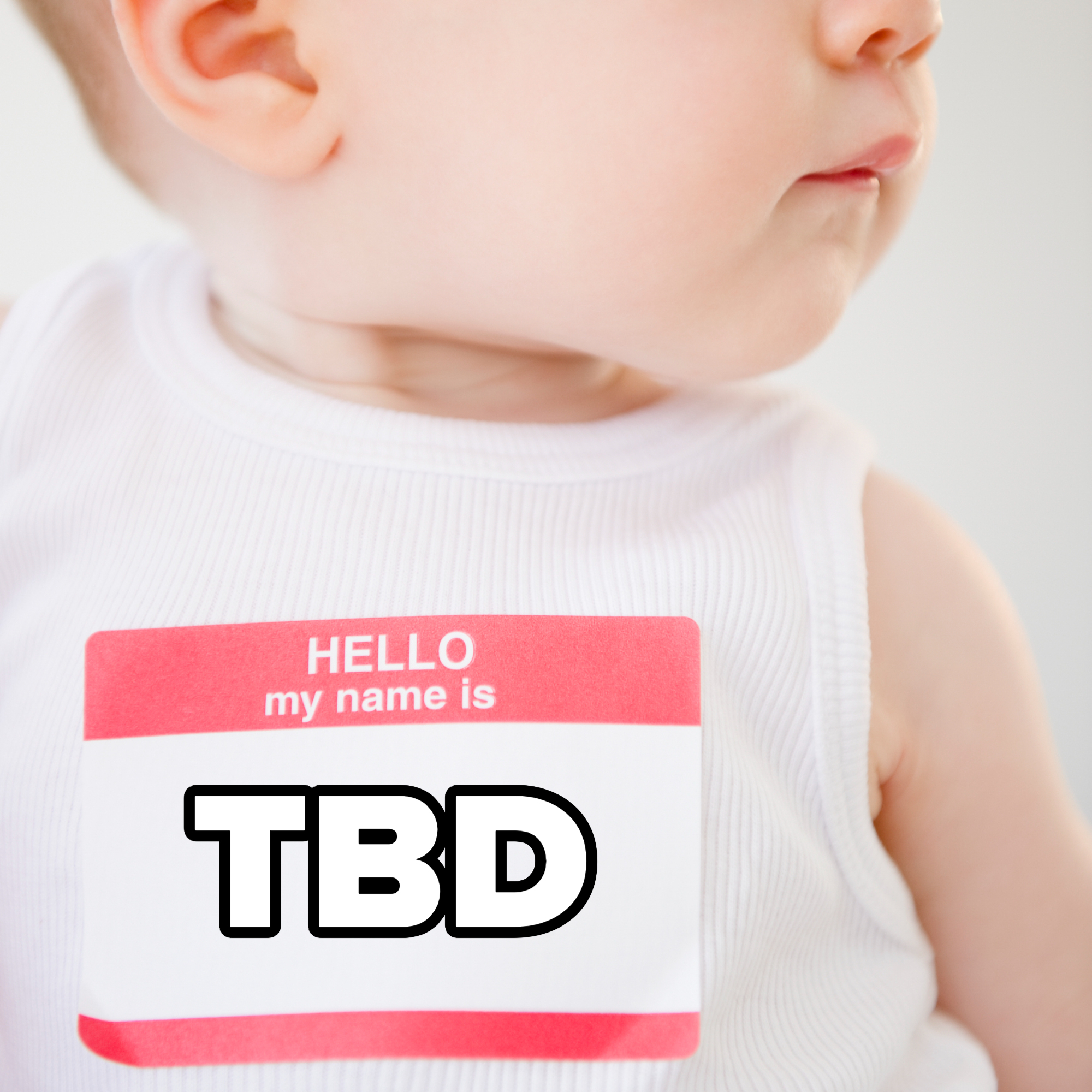An infant wearing a white sleeveless shirt looks to the right, with a blank name tag sticker that reads "Hello, my name is" on the shirt