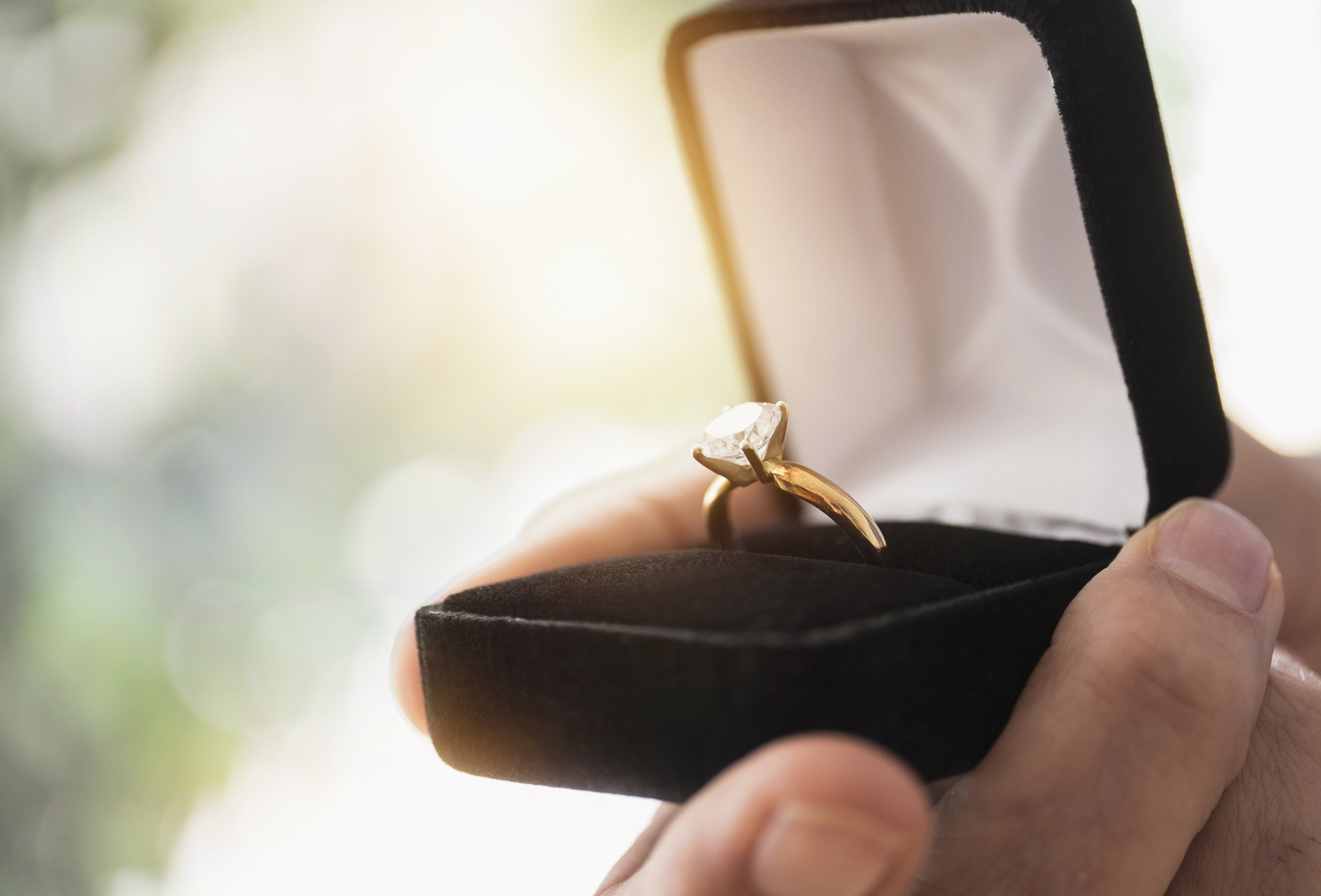 A closeup of hands holding an open ring box with a diamond engagement ring inside