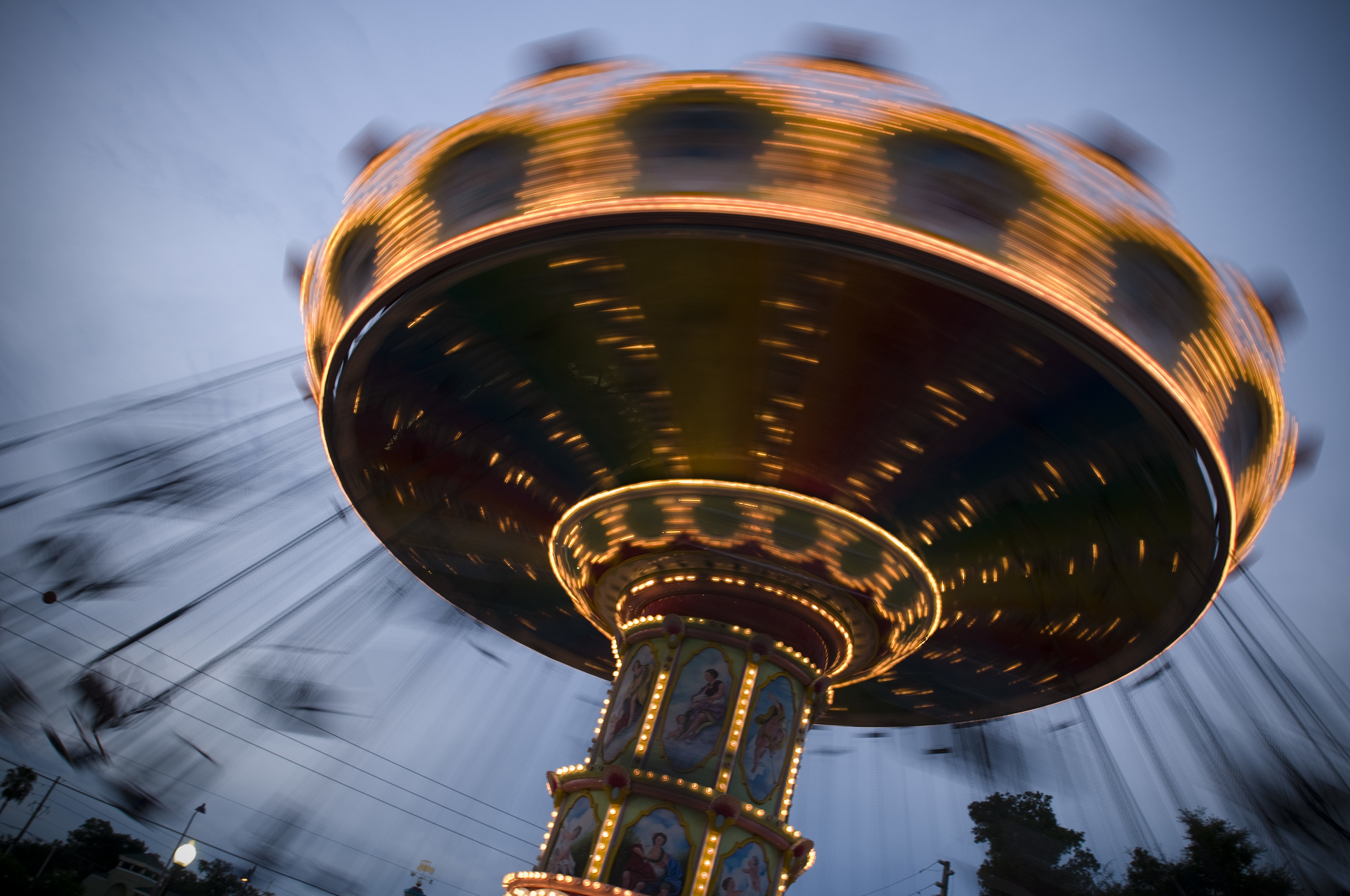 A brightly lit spinning carnival swing ride blurs with movement, creating an enchanting and dynamic atmosphere against the evening sky