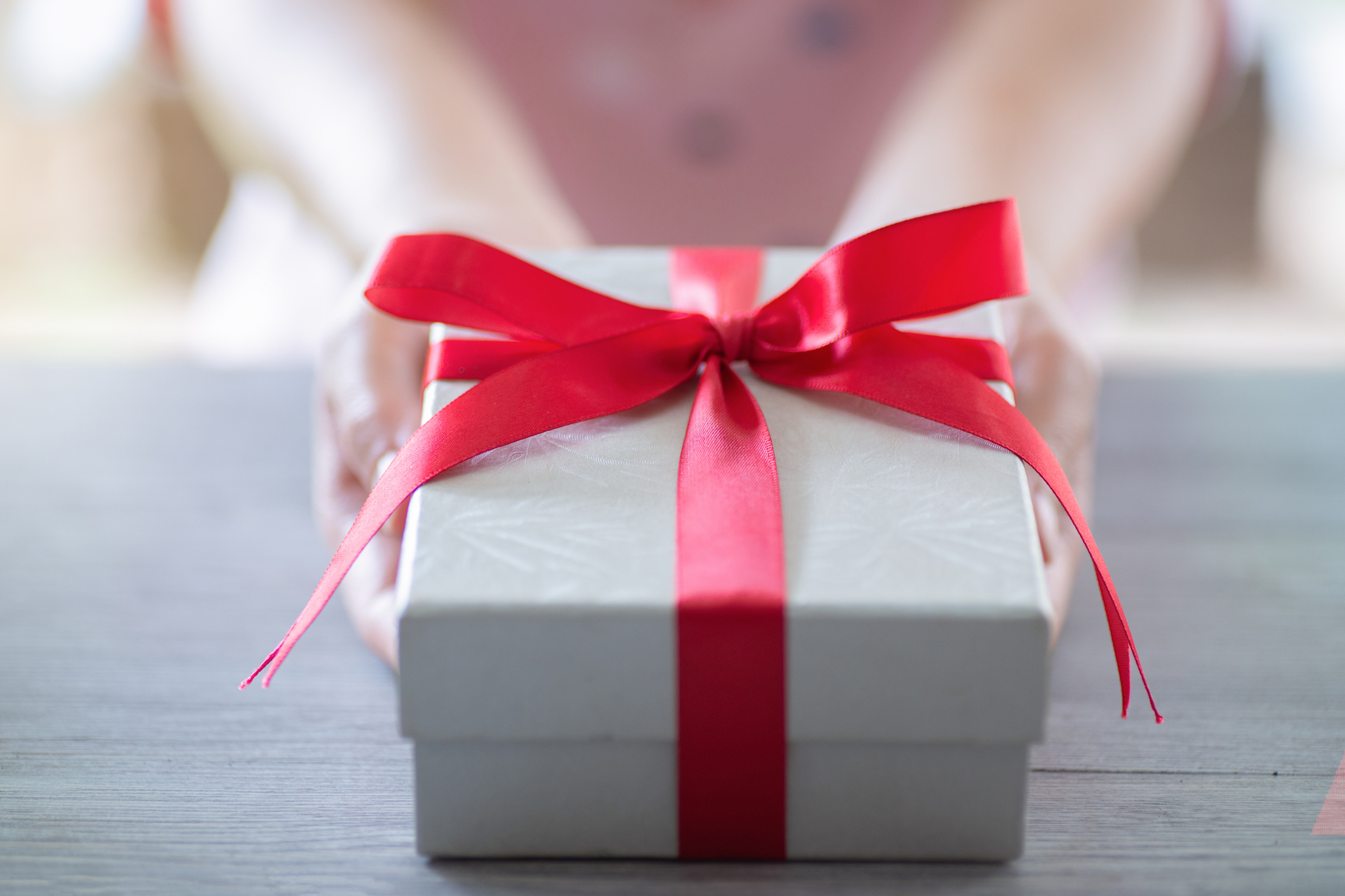 Person holding a white gift box tied with a red ribbon. The image has a romantic context, suitable for an article on relationships