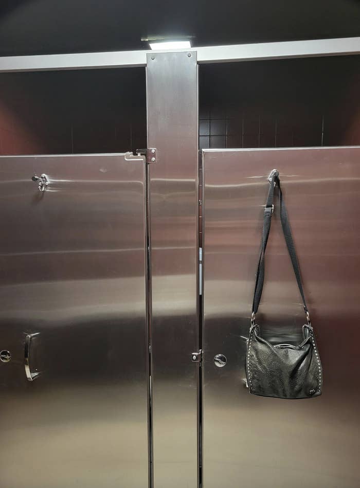 A handbag is hanging on the metal partition of a public restroom stall