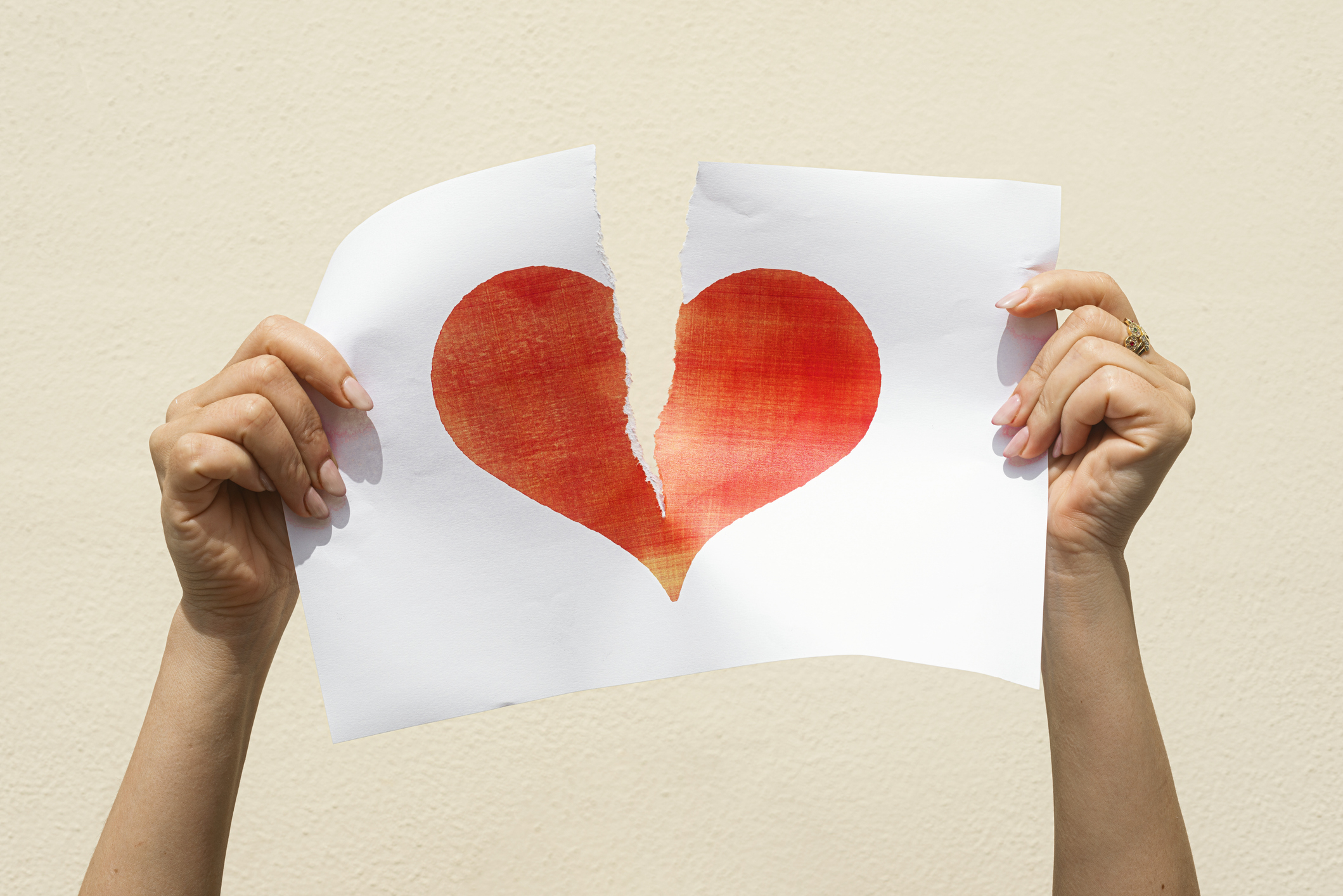A pair of hands holding two torn halves of a paper with a heart drawn on it