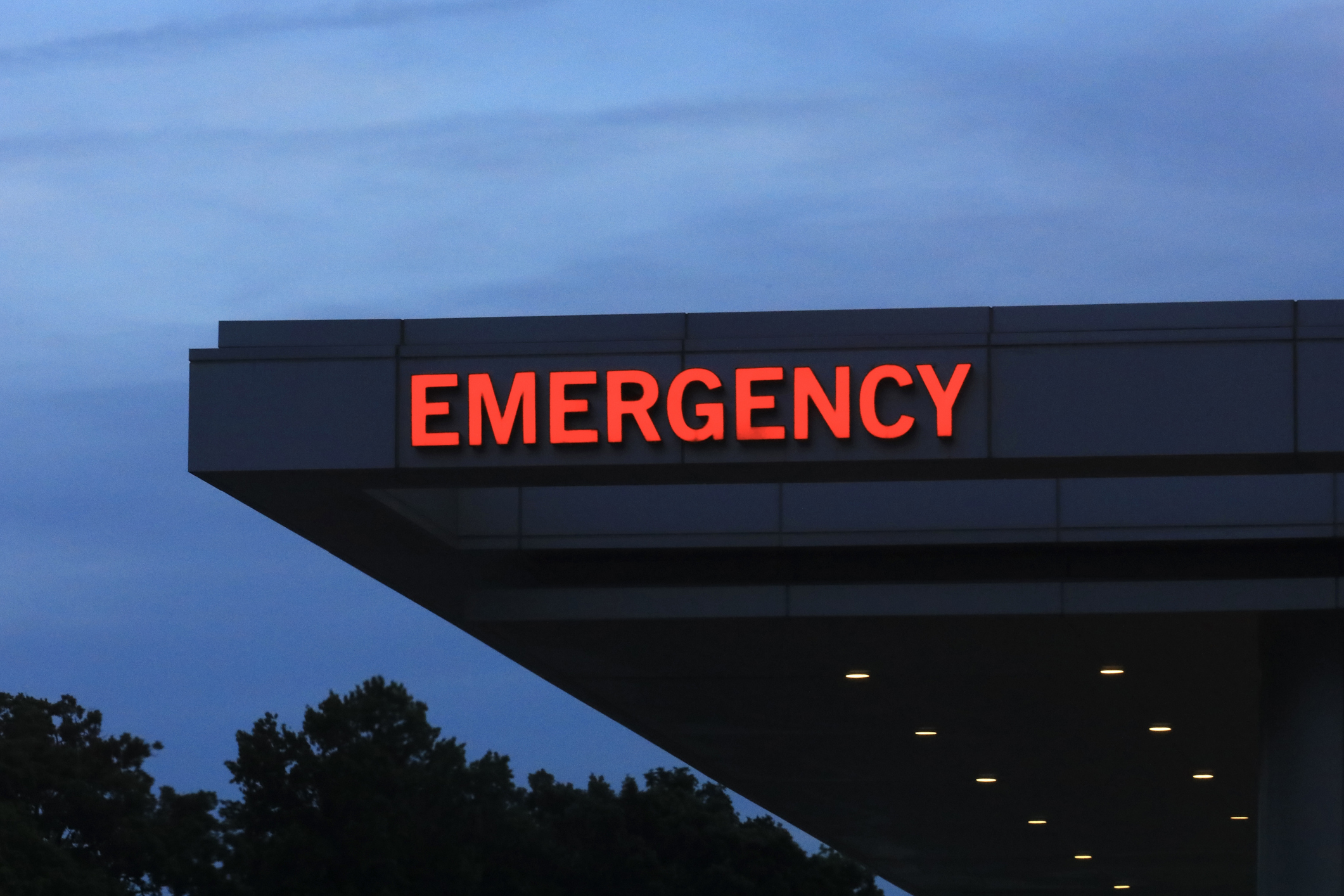 A building with a prominent red &quot;EMERGENCY&quot; sign on its exterior, photographed during twilight