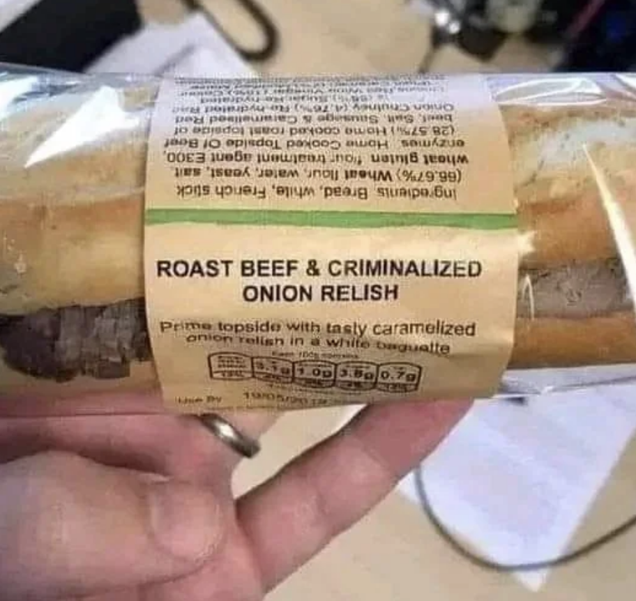 A hand holding a packaged sandwich labeled "Roast Beef & Criminalized Onion Relish" instead of "Caramelized Onion Relish."