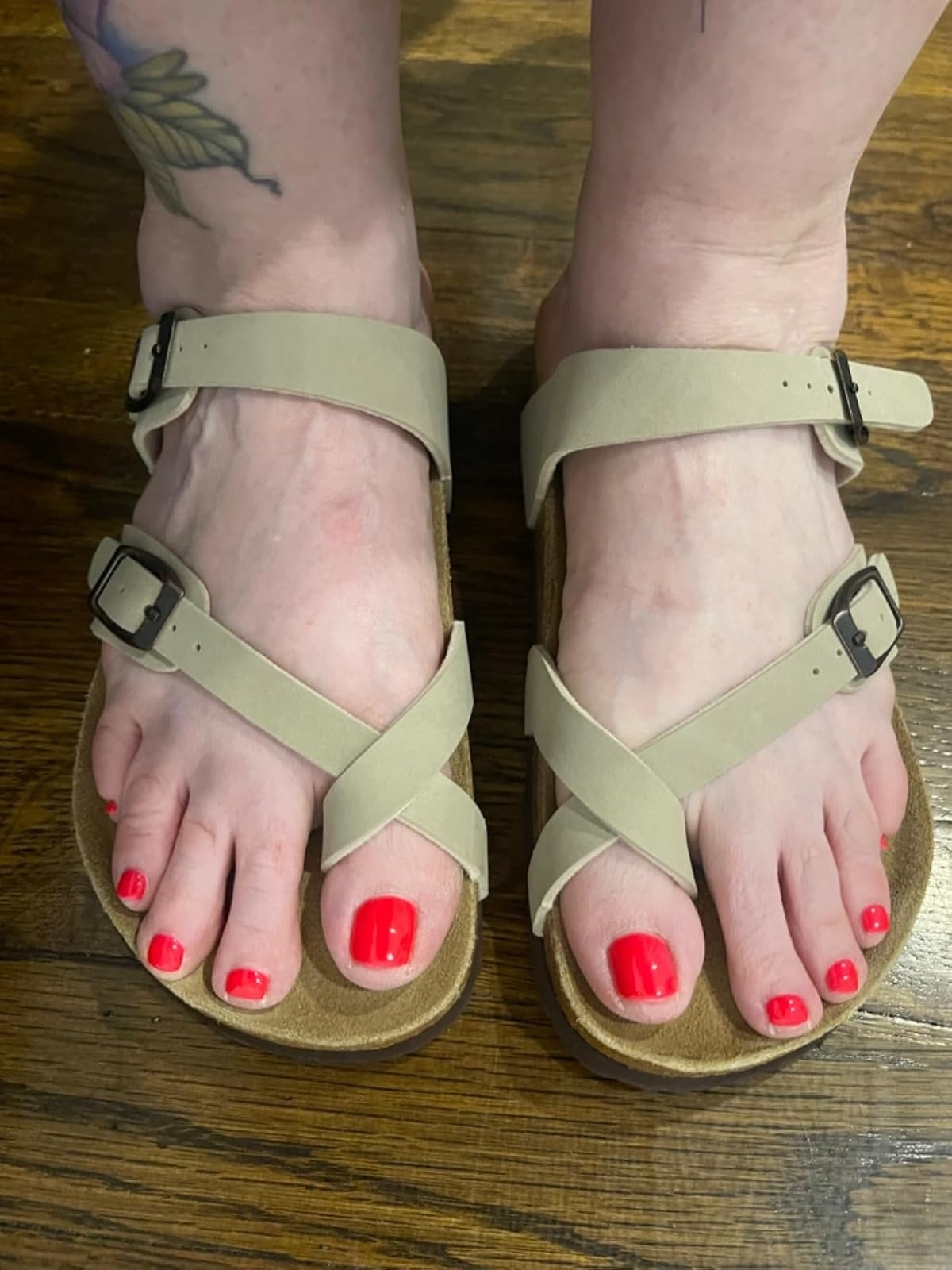 Reviewer's photo of them wearing beige sandals with buckles, showcasing a fresh red pedicure. There's a tattoo visible on the right ankle