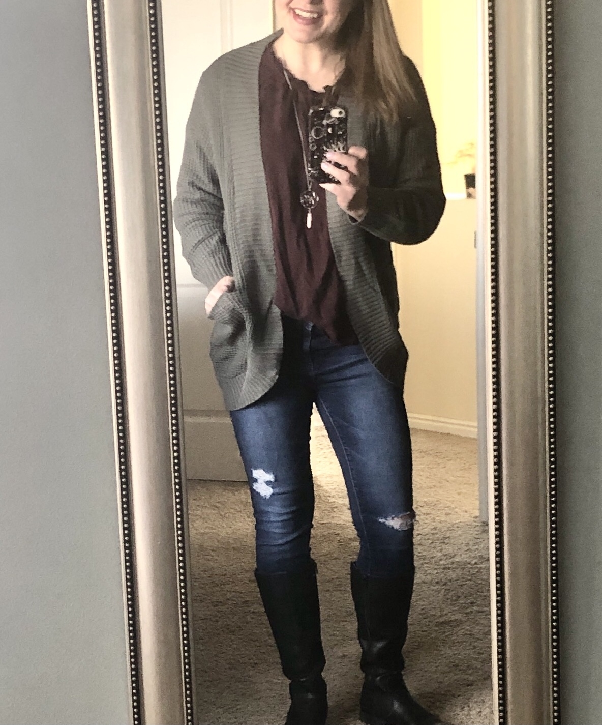 Reviewer's photo of them in a mirror selfie wearing a casual outfit: a dark top, gray cardigan, ripped jeans, and knee-high black boots