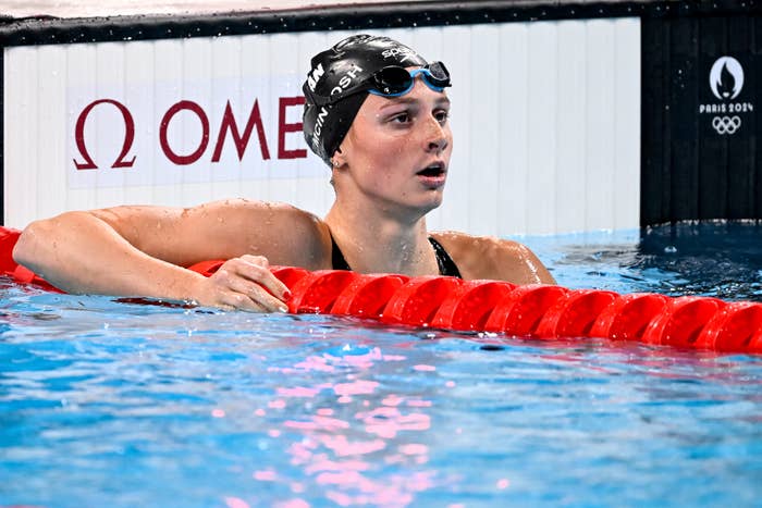 Swimmer Summer McIntosh, wearing a black cap and goggles, rests at the edge of a pool after a race in the Olympics