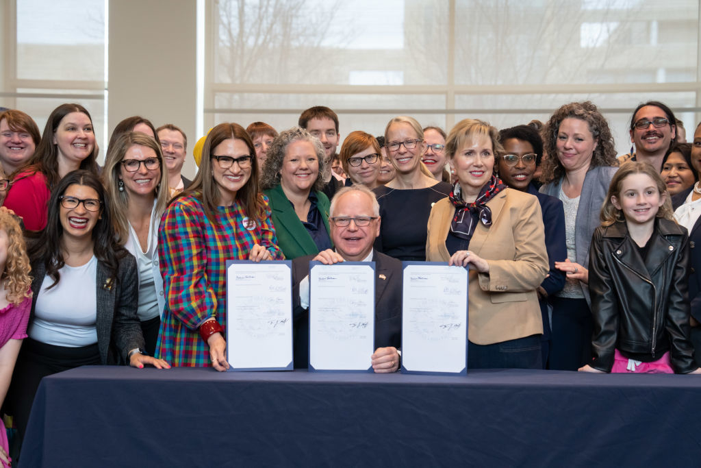 Group of smiling adults and children, two holding signed documents alongside Governor Walz