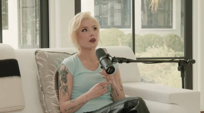 Halsey sits on a white couch in a bright room, speaking into a microphone. She wears a sleeveless top and black pants, showcasing arm tattoos
