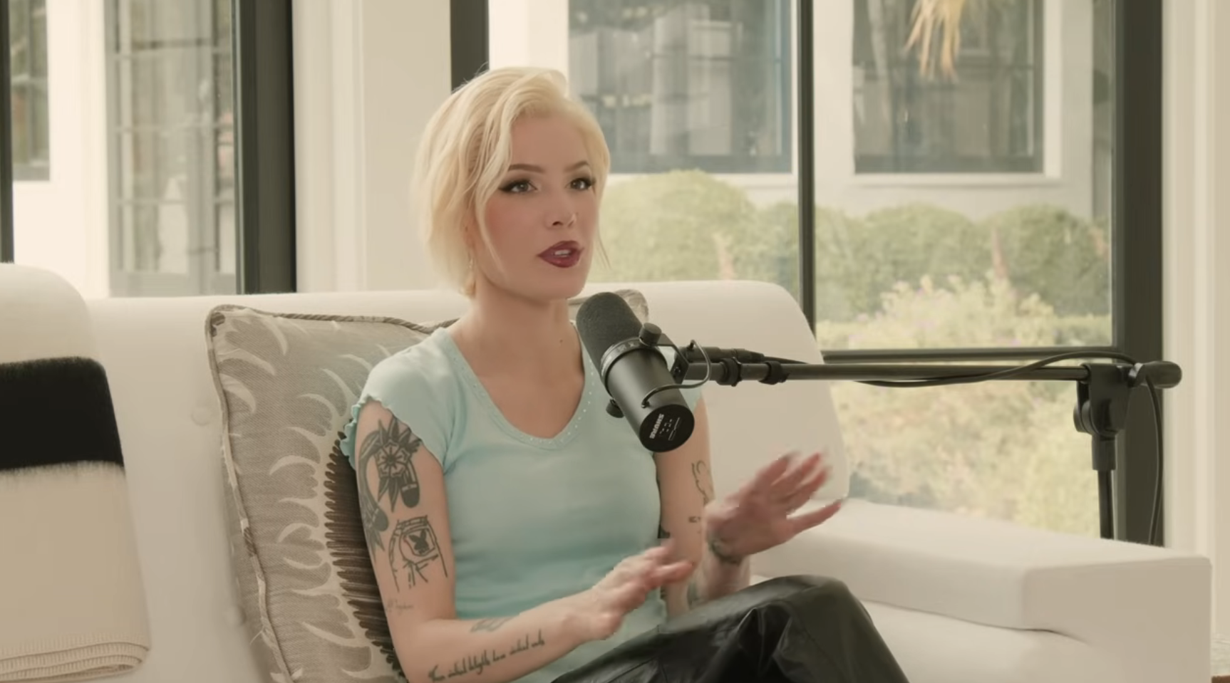 Halsey, in a casual outfit with visible tattoos, is seated on a sofa speaking into a microphone during an interview