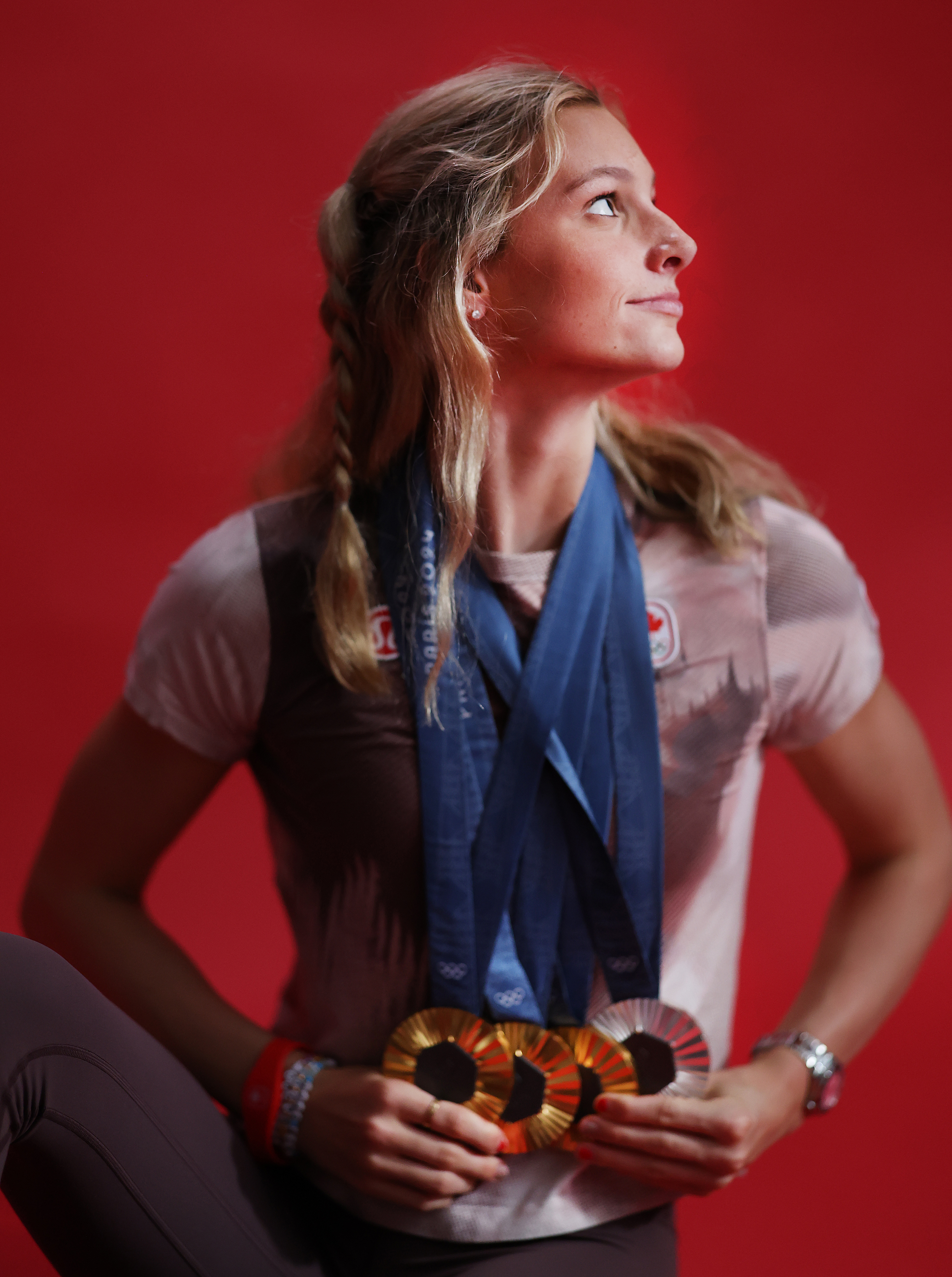 Athlete with braided hair proudly looks to the side, wearing multiple medals around her neck