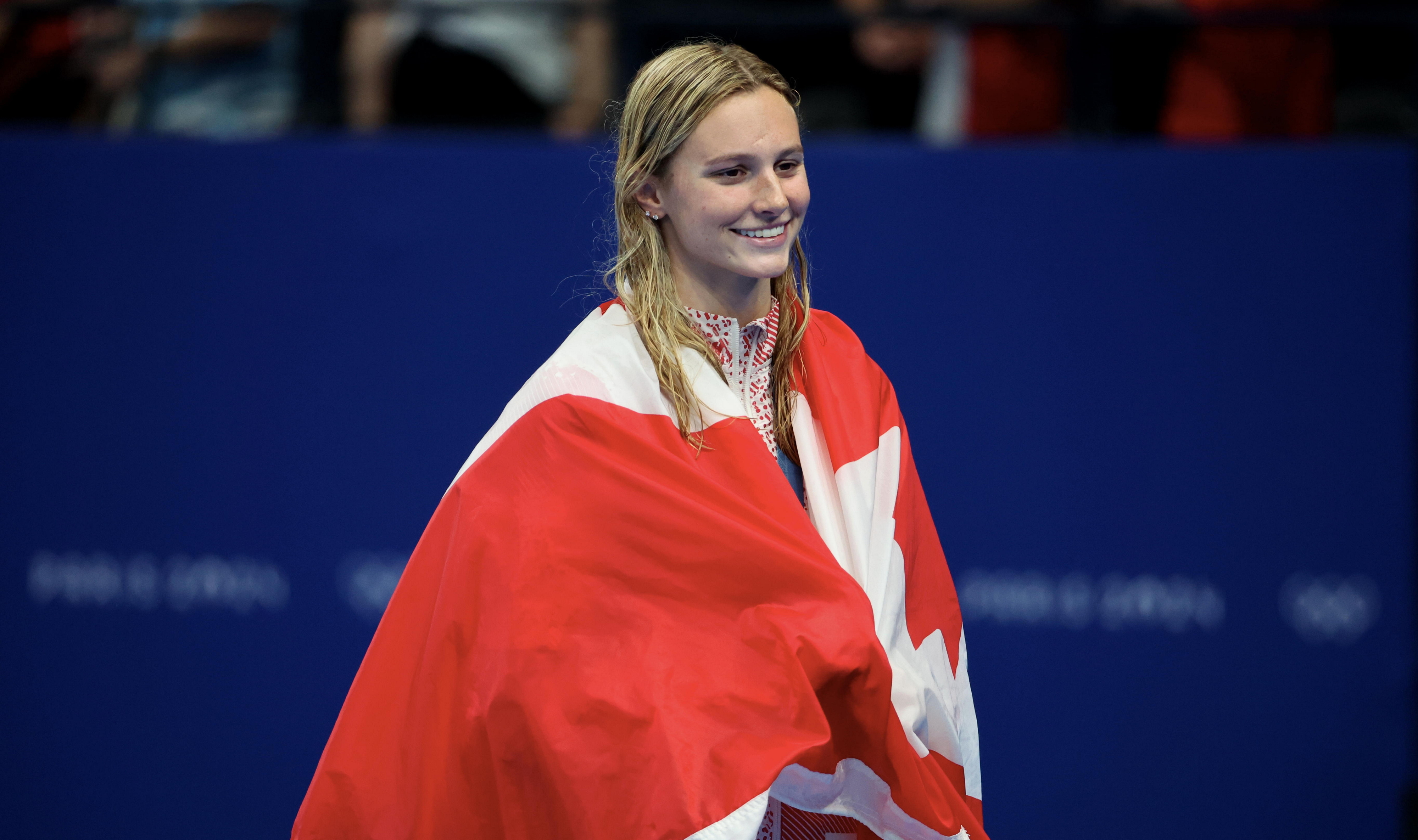 Smiling swimmer Maggie Mac Neil draped in a Canadian flag after winning an event at the 2020 Tokyo Olympics