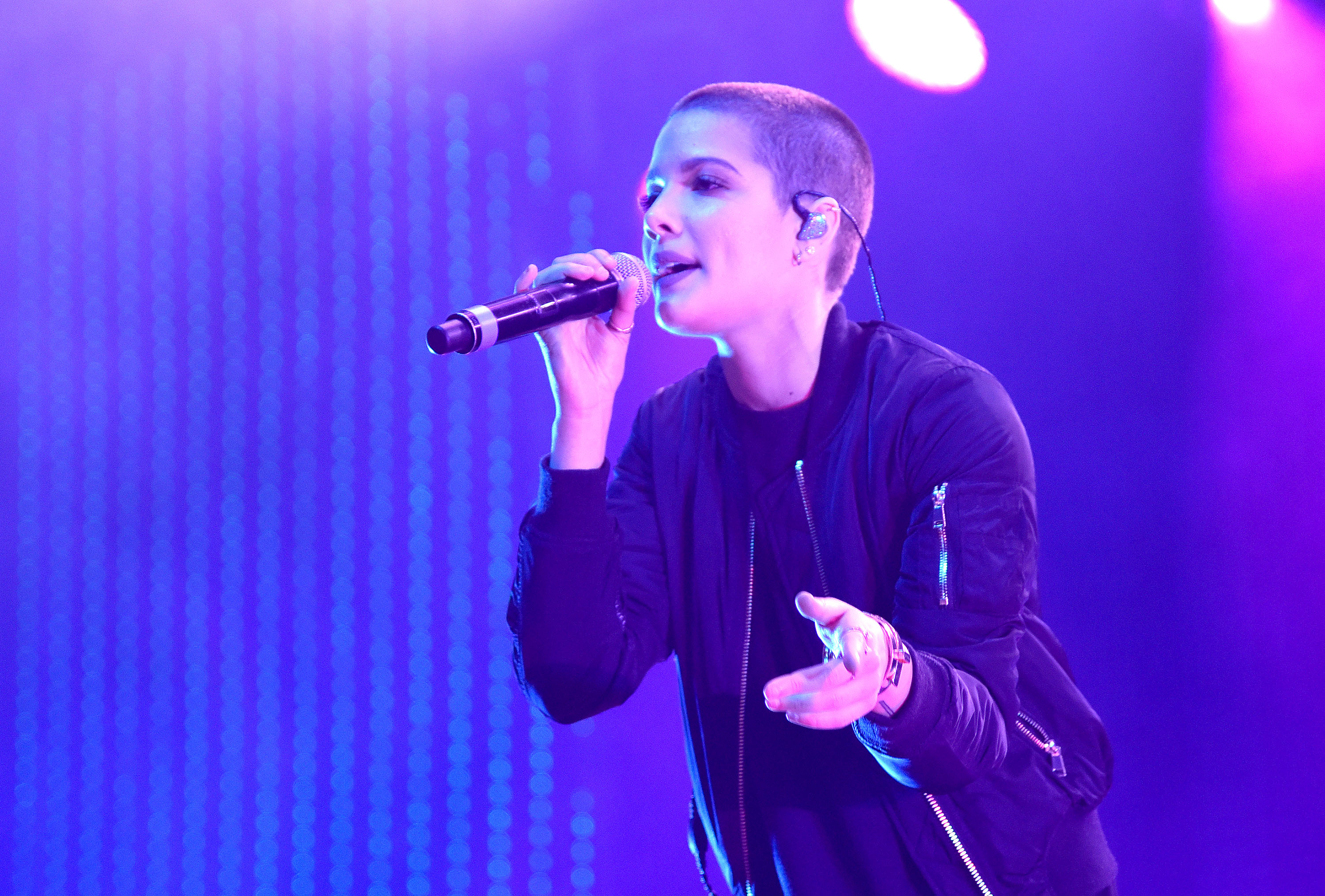 Halsey performs passionately on stage, wearing a sleek jacket and holding a microphone, creating an engaging connection with the audience