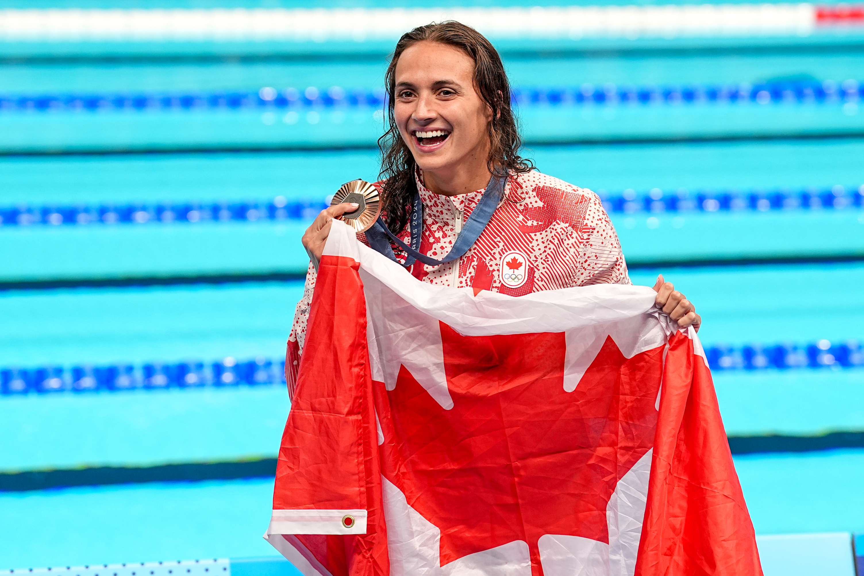 Olympic swimmer proudly holds a medal and a Canadian flag at the poolside