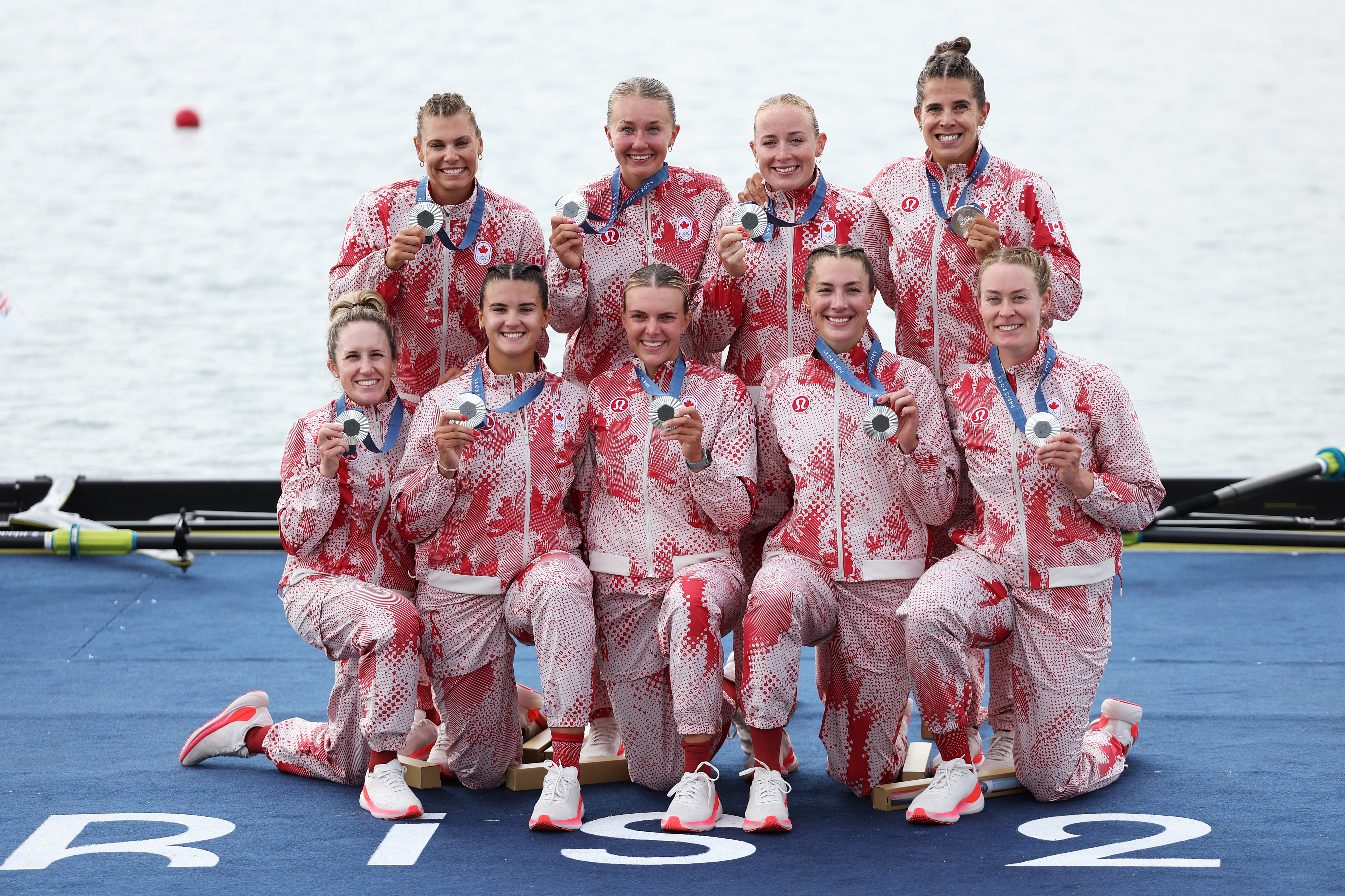 A team of female rowers, all wearing matching sportswear, smiles and holds their medals while posing for a group photo after a competition