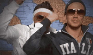 Two men in athletic jackets and sunglasses are dancing enthusiastically in front of a map. One has "Italia" written on his jacket. Names unknown