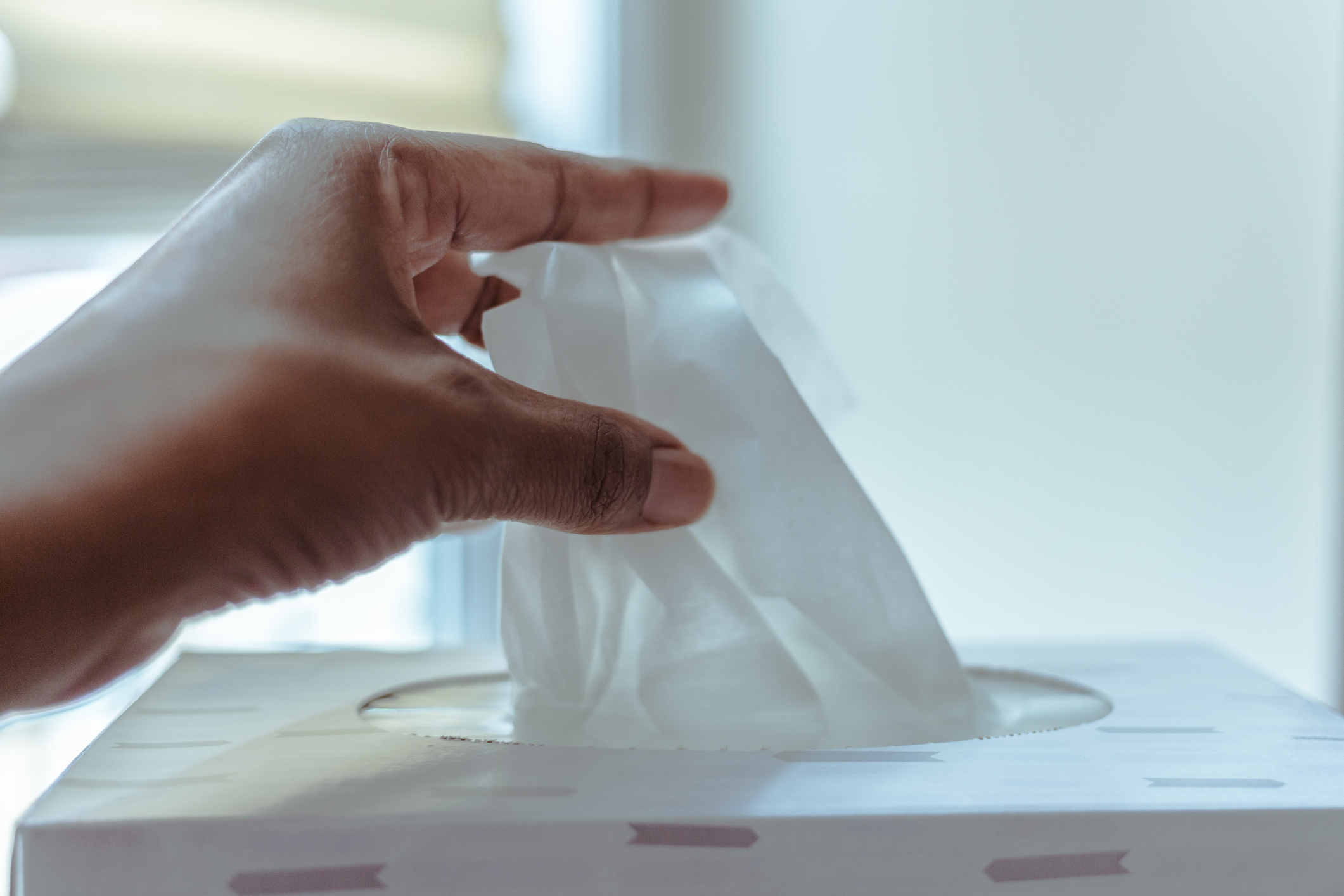 A hand reaches for a tissue from a tissue box