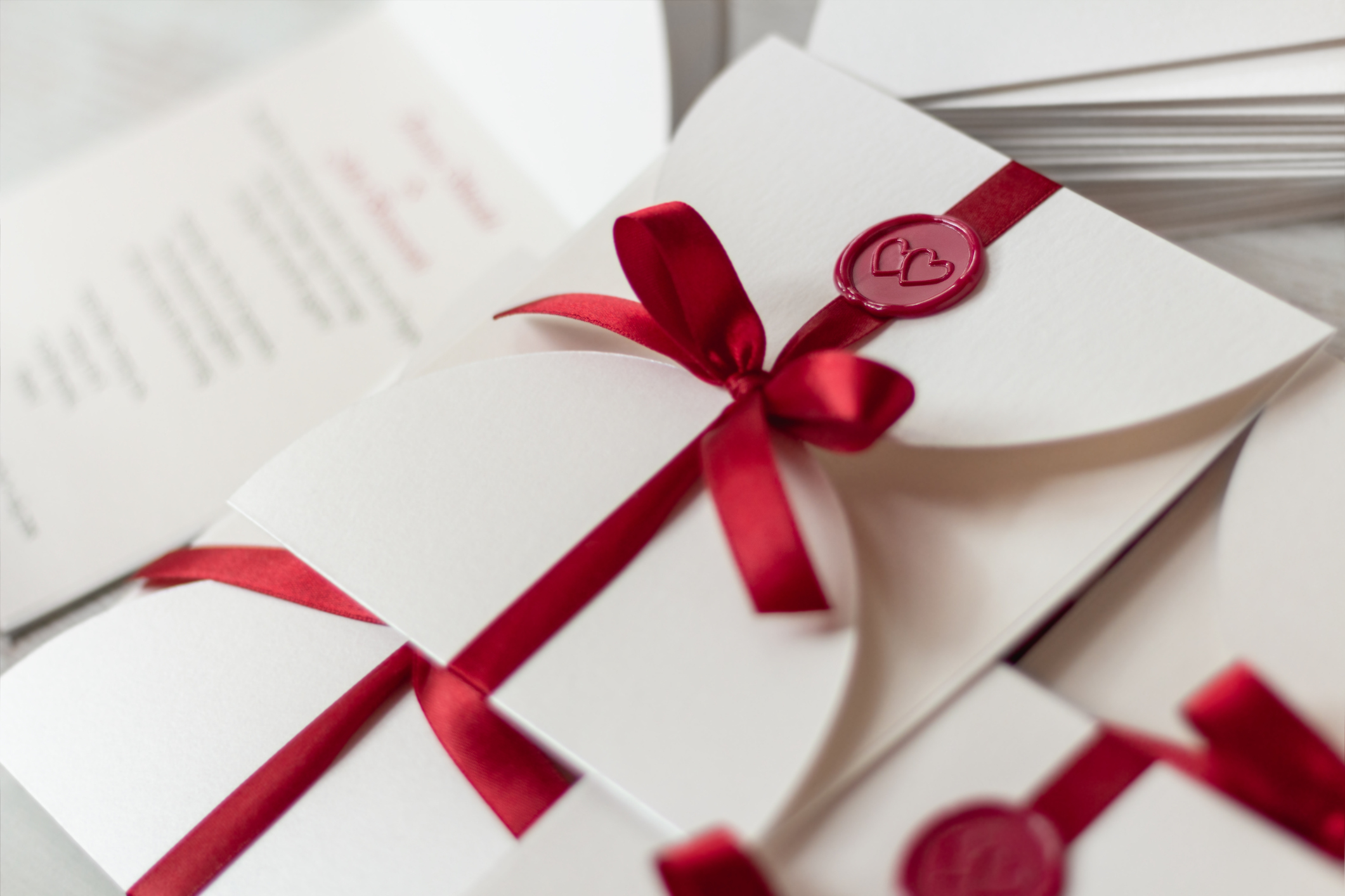 A stack of elegant wedding invitations with red ribbons and wax seals, featuring folded cards tucked inside