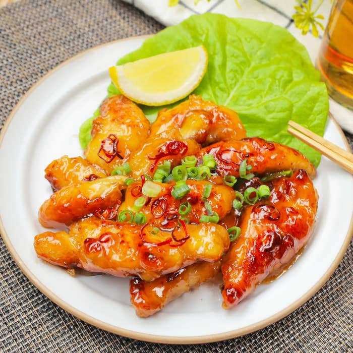 お皿に盛り付けられた、ネギが散らされた照り焼きチキンとレタス、レモンのくし型が添えられた料理。