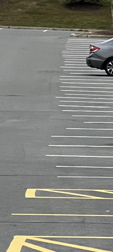 Partially empty parking lot with a single sedan parked in one of the spaces