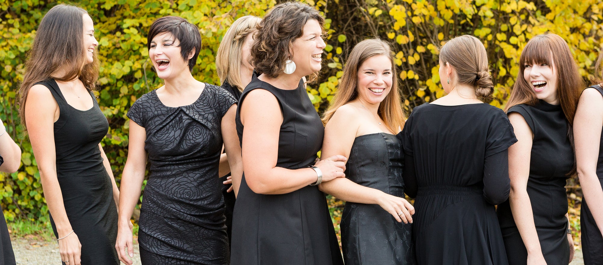 A group of women dressed in black dresses, smiling and laughing at an outdoor wedding event. Names of the women are unknown