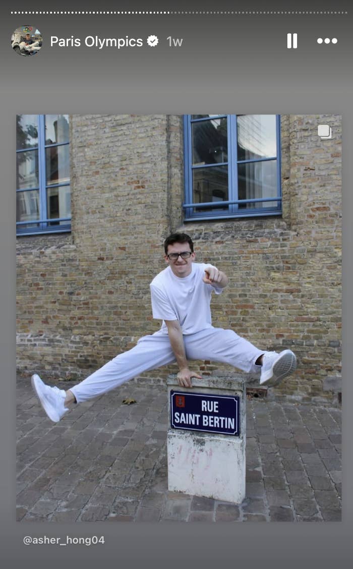 Asher Hong, dressed casually, performs a split jump over a street sign reading "Rue Saint Bertin."