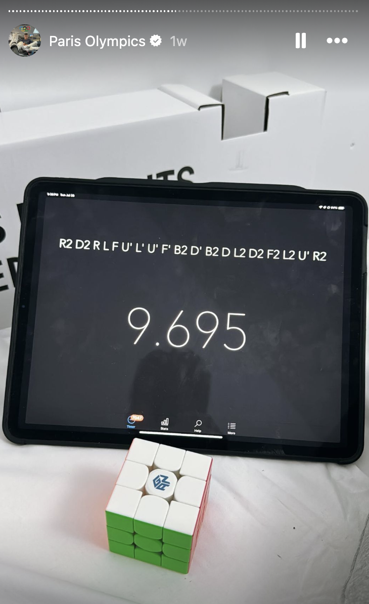 An iPad displays "9.695" with a sequence of Rubik's Cube moves above it. A solved Rubik's Cube is placed in front of the iPad