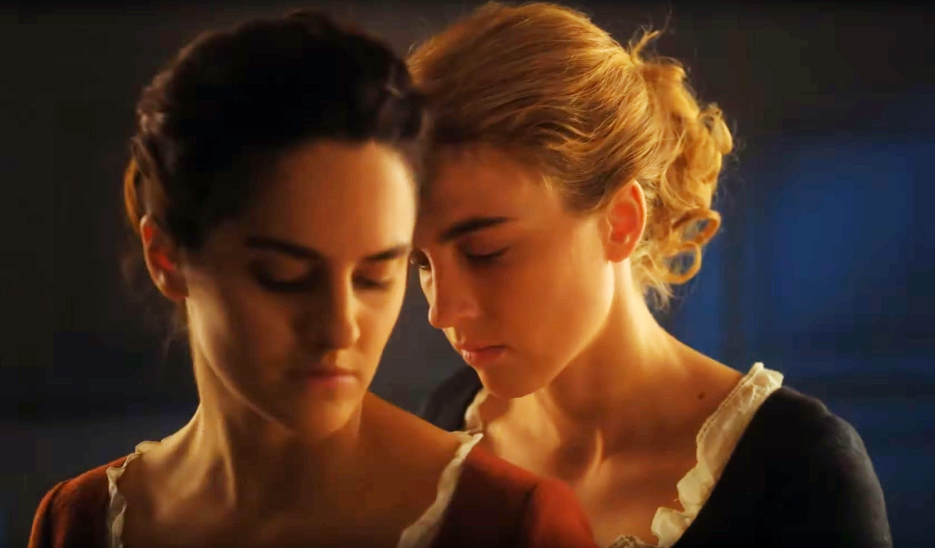 Adèle Haenel and Noémie Merlant in a close, intimate moment from the movie "Portrait of a Lady on Fire". Adèle stands behind Noémie with her head on her shoulder