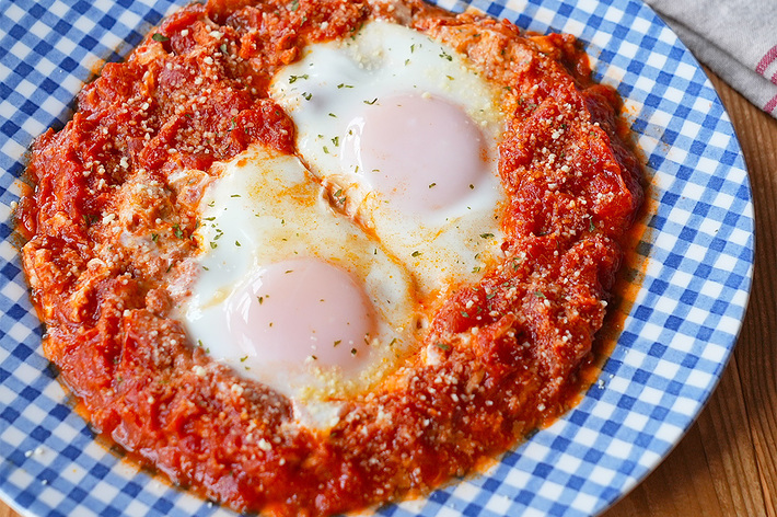 チーズとトマトソースの上に、2つの卵がのった焼き料理がチェック柄のプレートに盛られています。