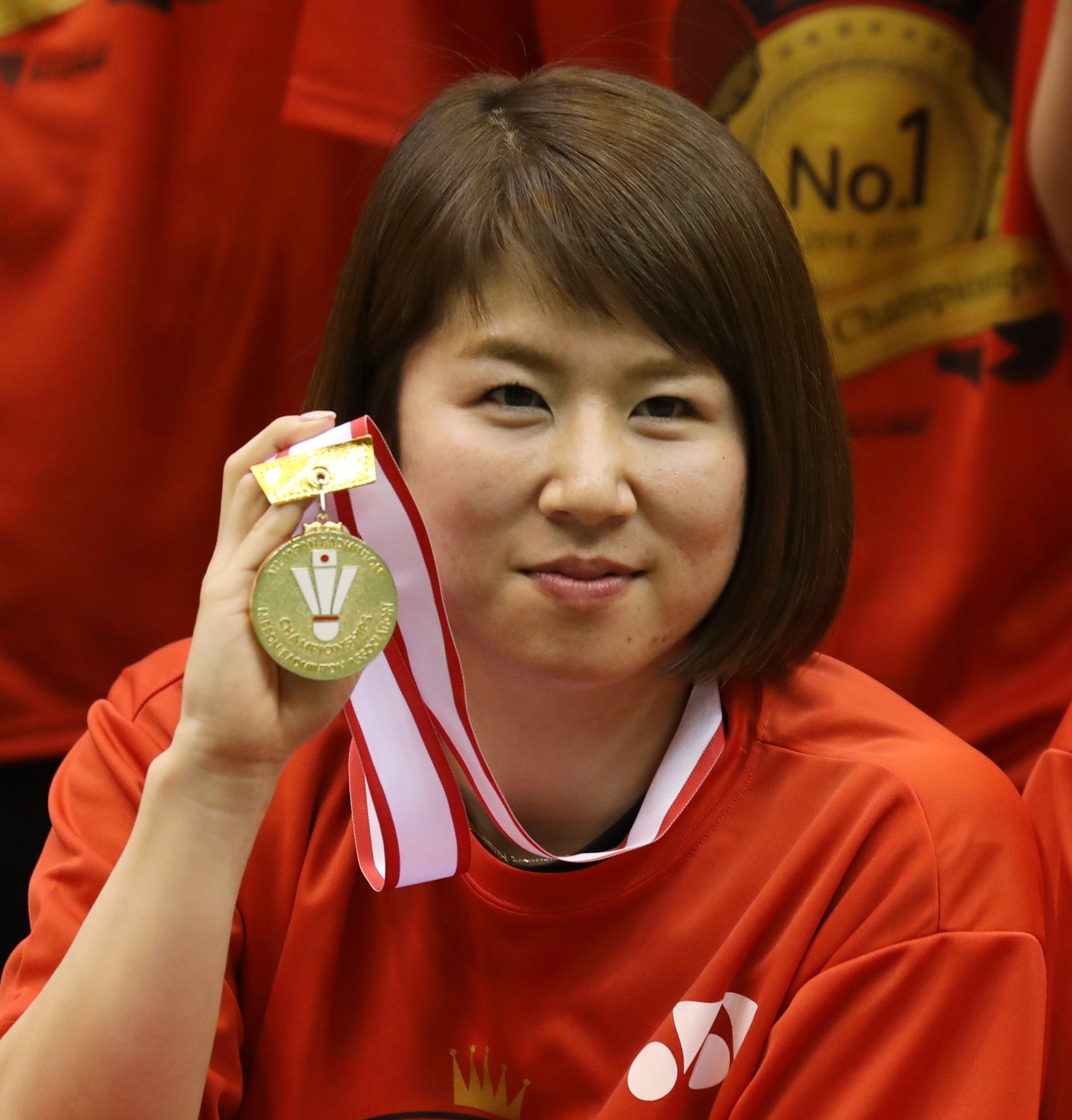 福島由紀と廣田彩花が金メダルを手にして並んでいます。背景には同じデザインのTシャツを着た他の選手たちがいます。