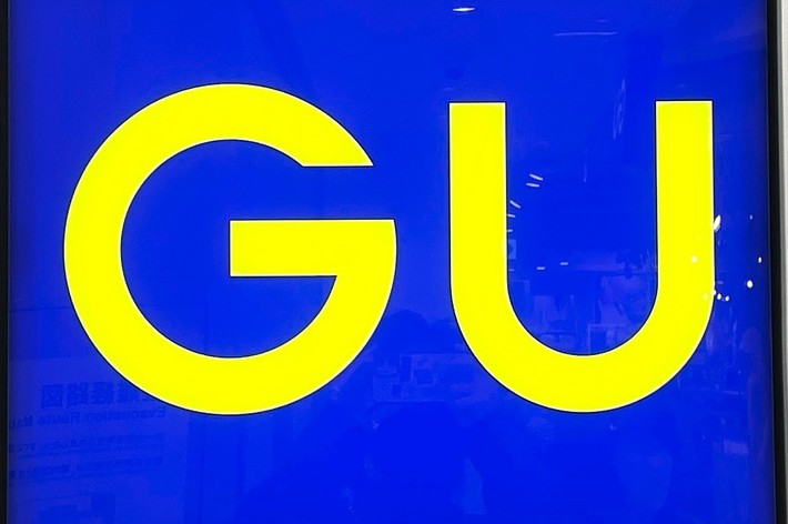 Illuminated square sign with &ldquo;GU&rdquo; in large yellow letters. Background is a solid blue color