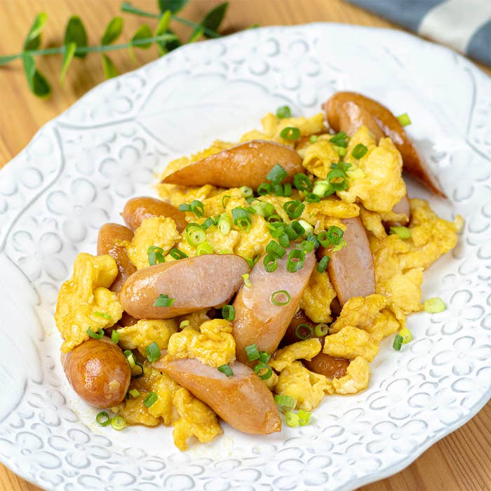 白い皿に盛り付けられたスクランブルエッグとウインナーの料理。刻んだネギが散らしてある。