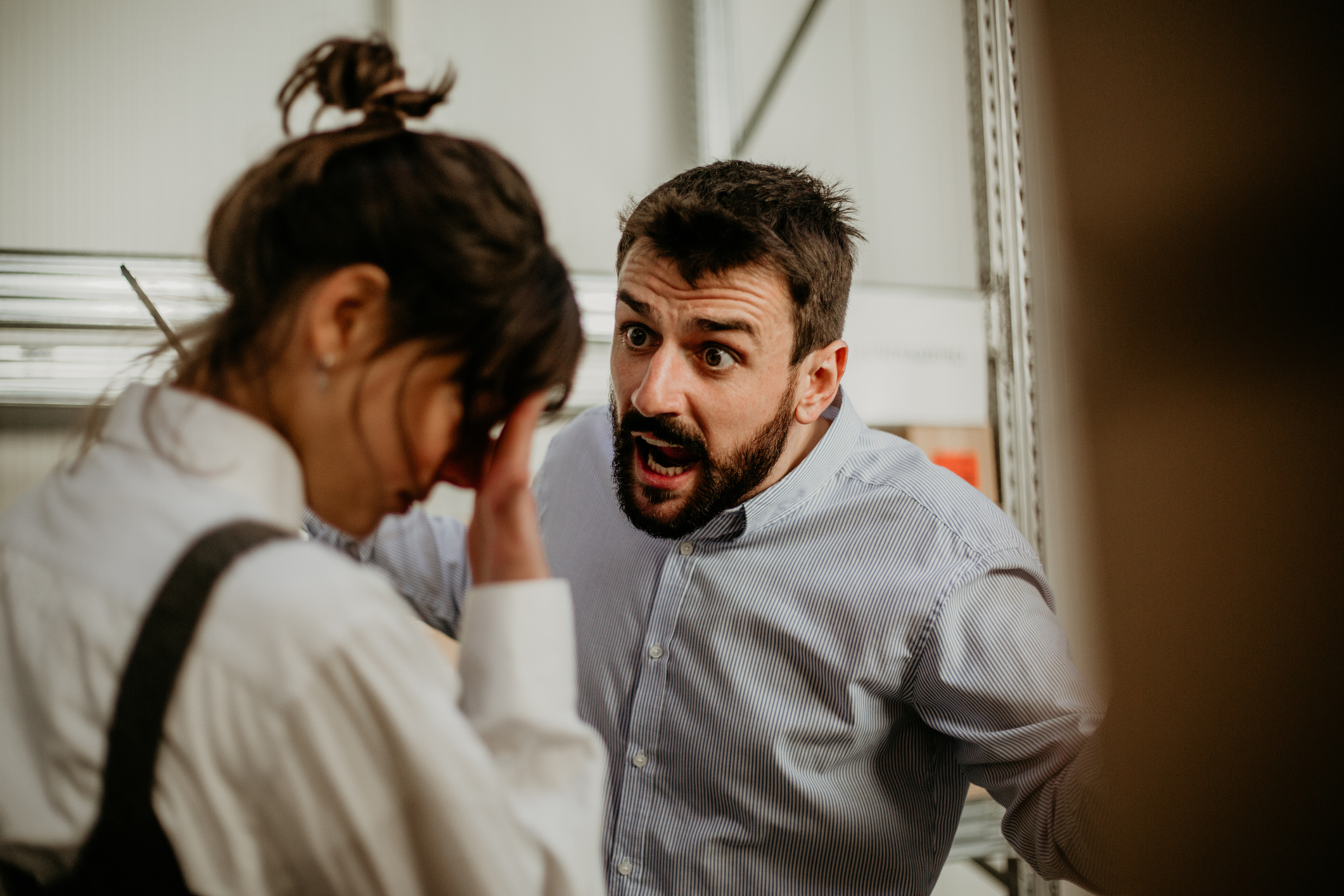 Man in a dress shirt appears to be angrily speaking to a woman with her head down, holding her forehead in a frustrated manner