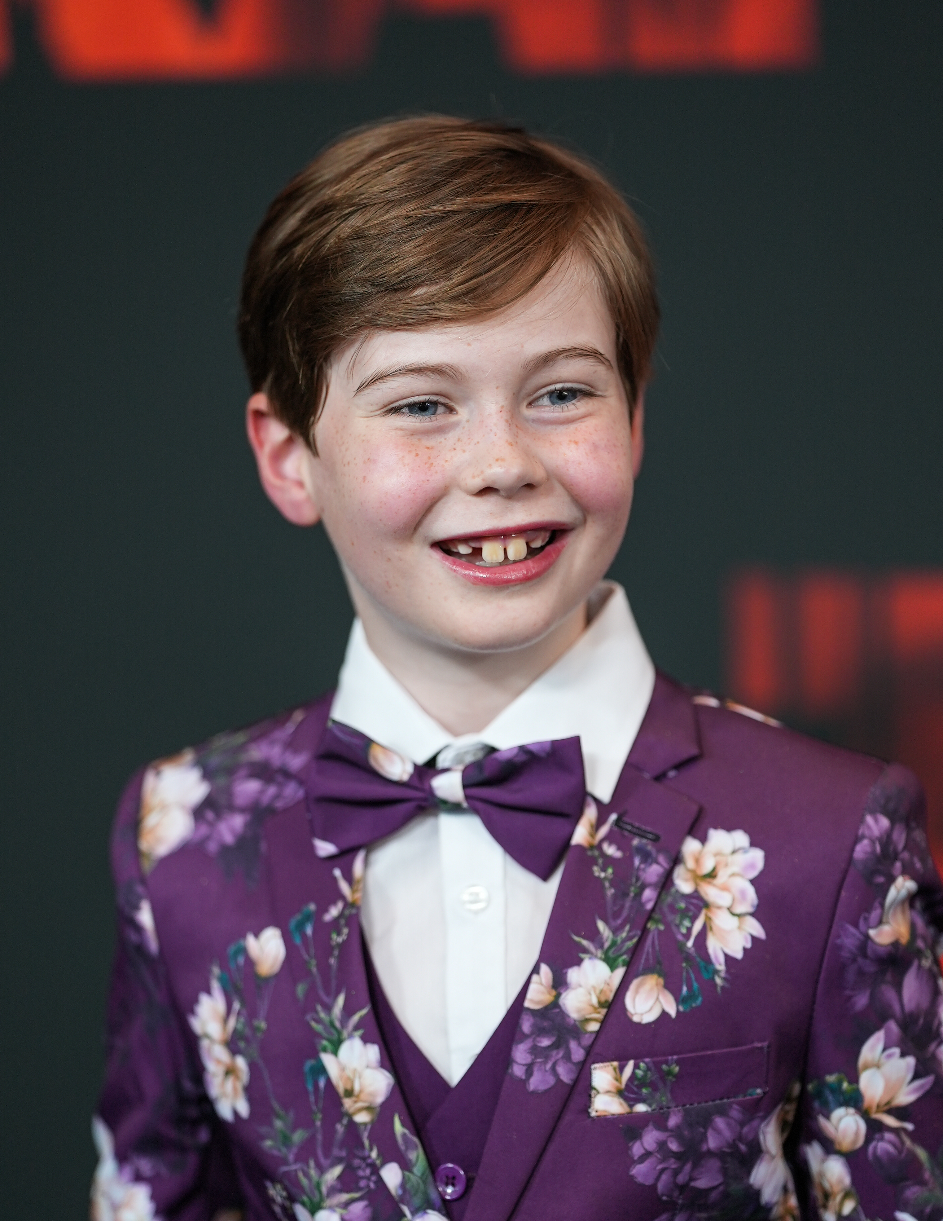 Lochlan Miller in a floral-patterned suit, bow tie, and white shirt is smiling on the red carpet