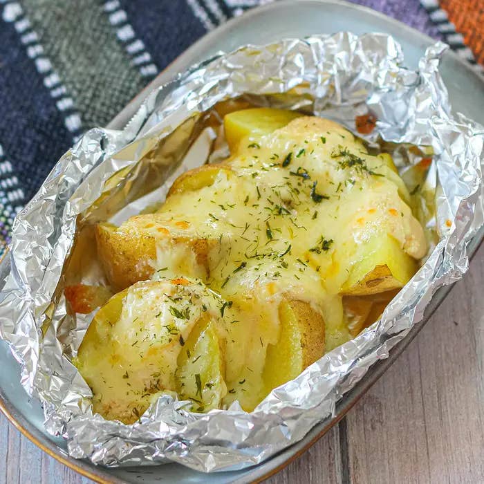 ホイルに包まれた焼きポテト、溶けたチーズとハーブがかかっている。