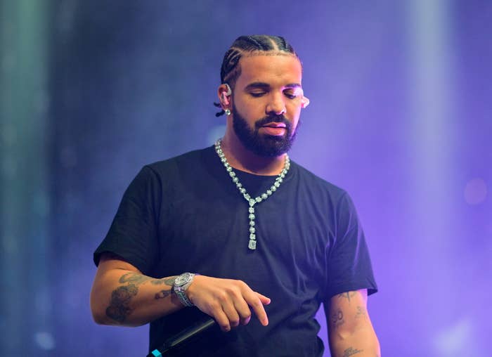 Drake performing on stage wearing a black T-shirt, a diamond necklace, and holding a microphone